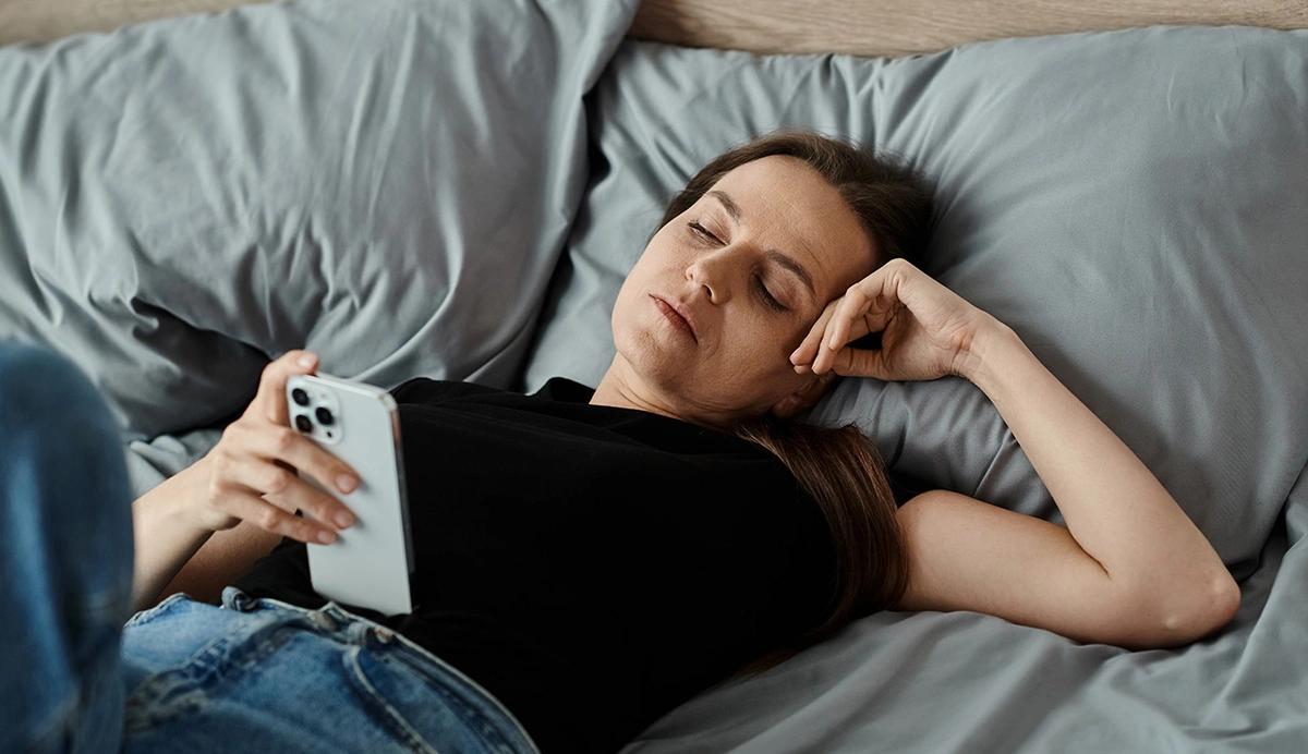 woman lying in bed scrolling on her phone